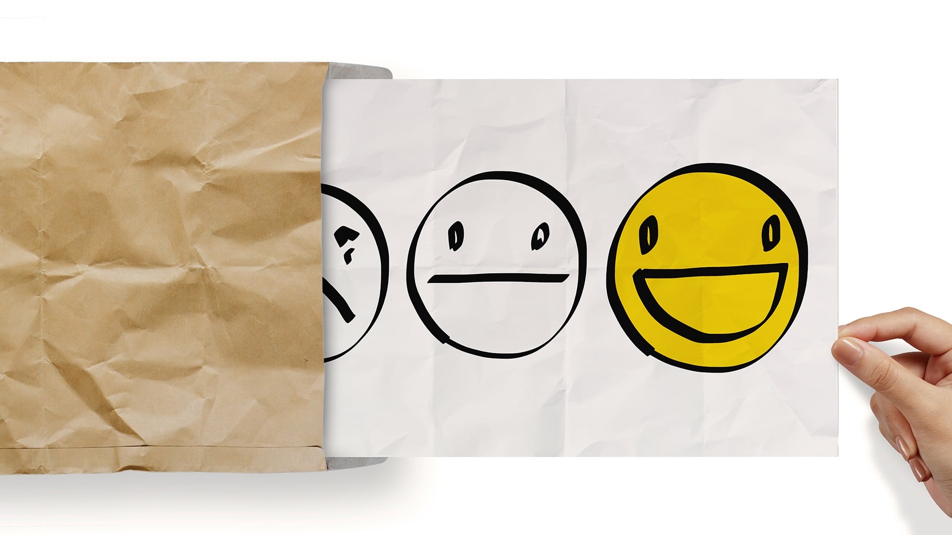 Een hand onthult een papier met drie getekende gezichten: een droevig gezicht aan de linkerkant, een neutraal gezicht in het midden en een vrolijk, gloeiend geel gezicht aan de rechterkant. Het papier komt uit een verfrommelde bruine envelop met de vermelding "jouw ideale volger.