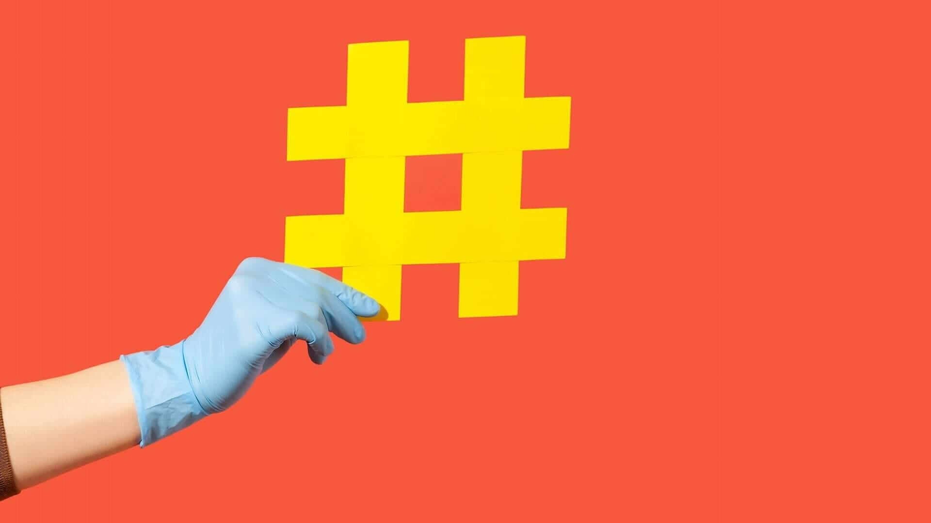 Een hand die een blauwe latex handschoen draagt, houdt een groot geel hashtag-symbool vast tegen een felrode achtergrond, wat illustreert hoe klanten via hashtags visueel aantrekkelijk kunnen zijn.