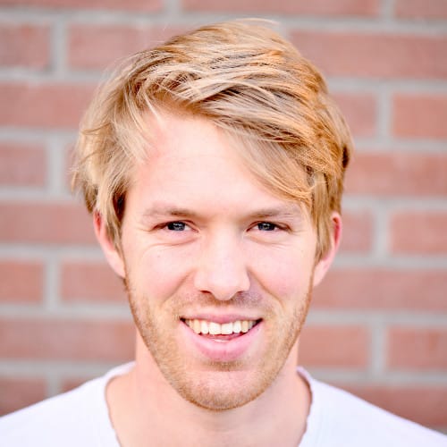 Een persfoto voor een stenen muur van een lachende blonde man voor social masterclass.