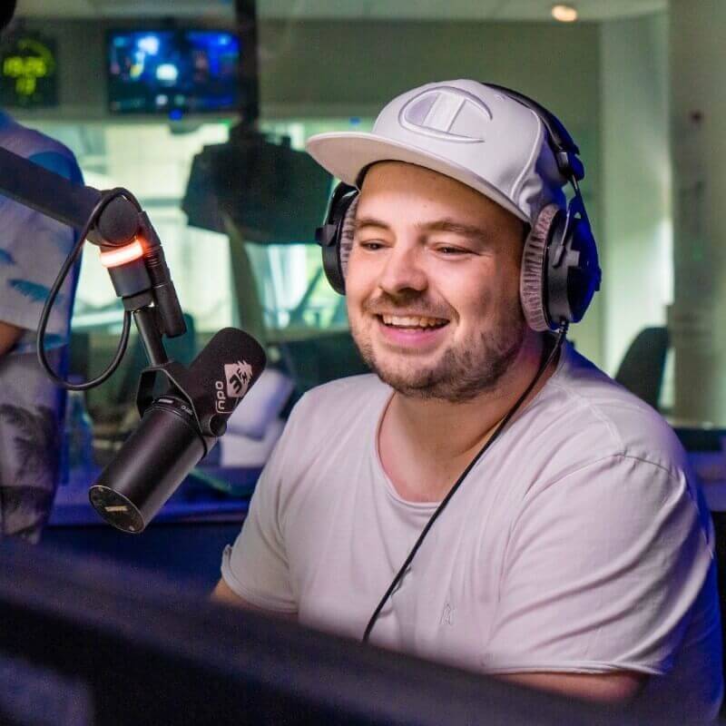 Een radio dj met een pet op in de studio van 3FM.